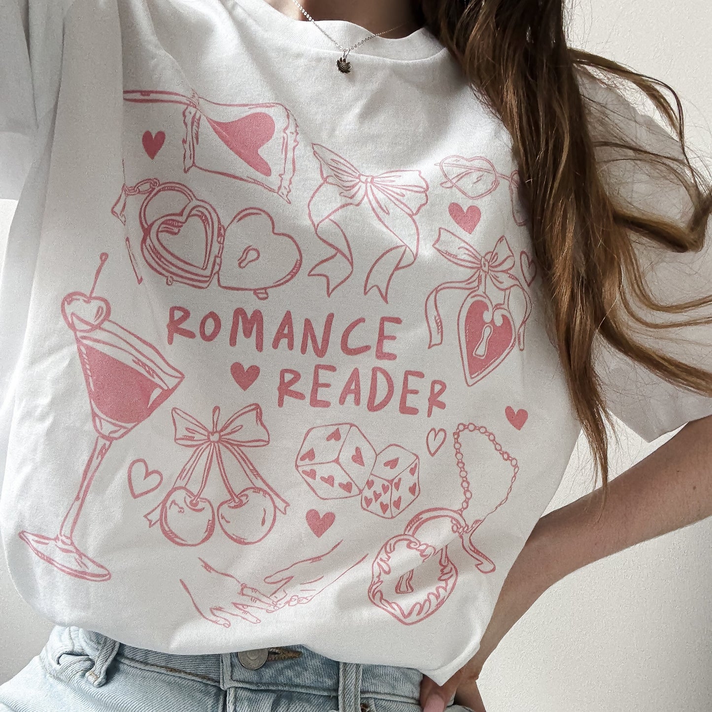 Person wearing a white t-shirt with pink 'ROMANCE READER' design and casual outfit.