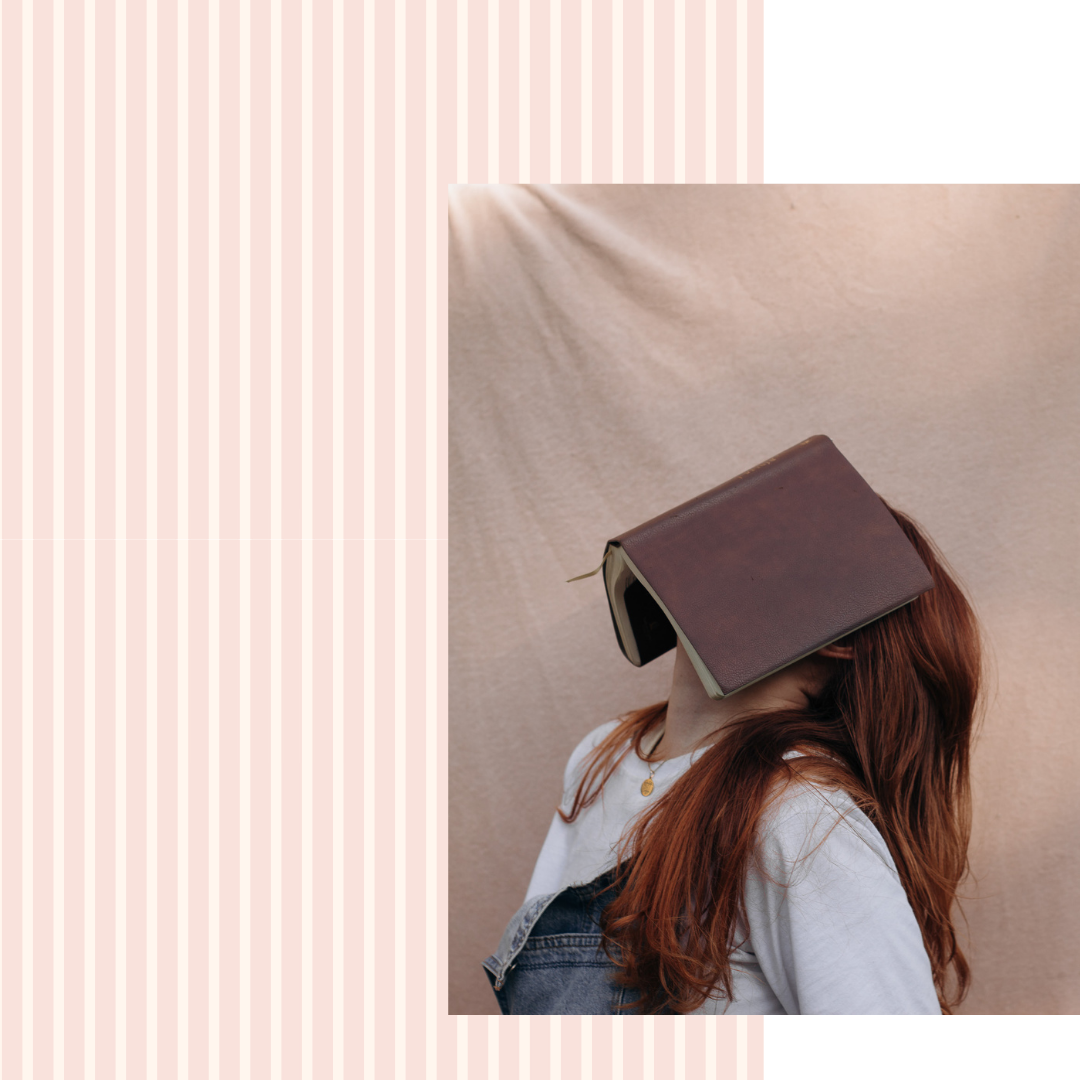 Person with a book covering their face against a plain background