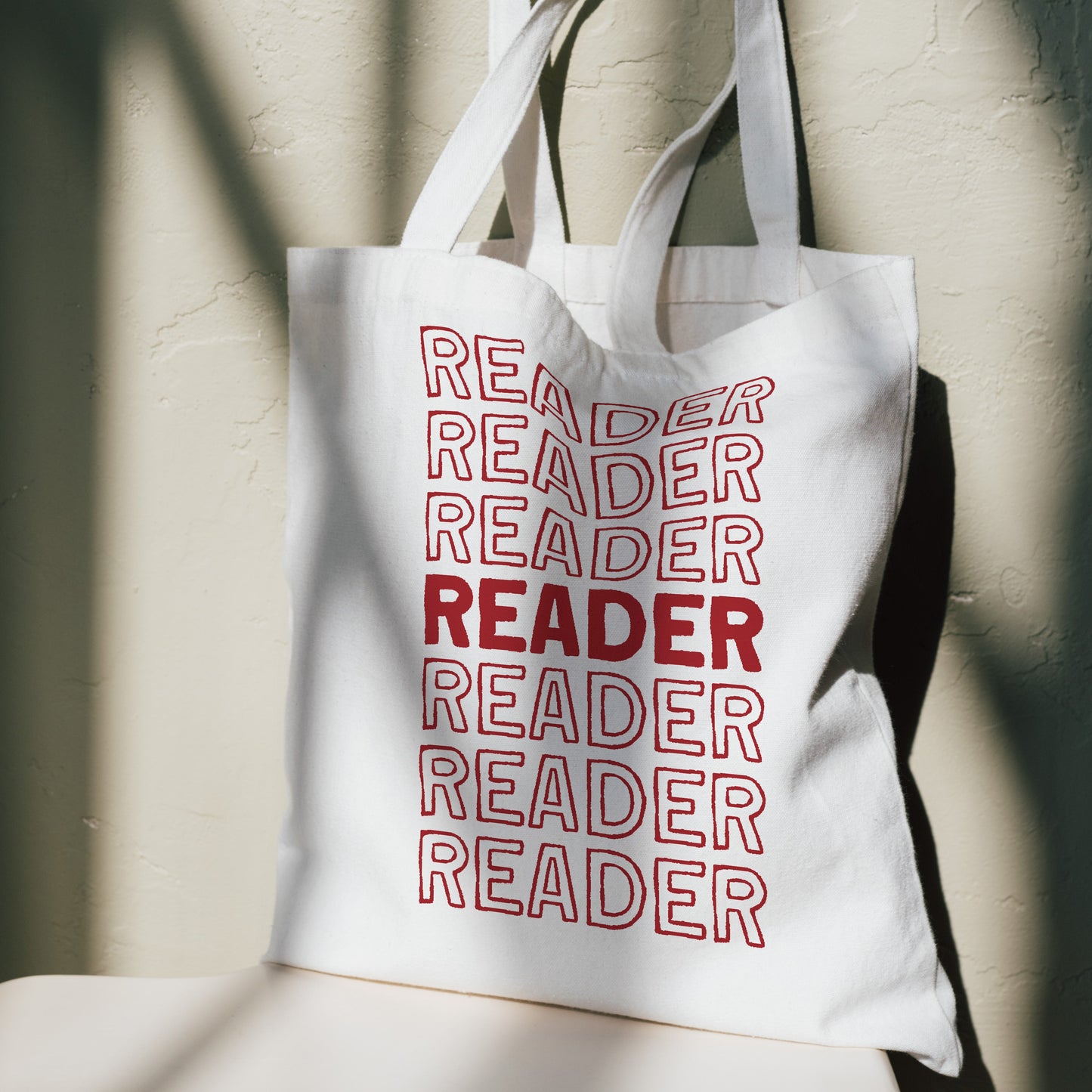 White tote bag with 'READER' text in red on a neutral background