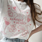 Person wearing a white t-shirt with pink 'ROMANCE READER' design and casual outfit.