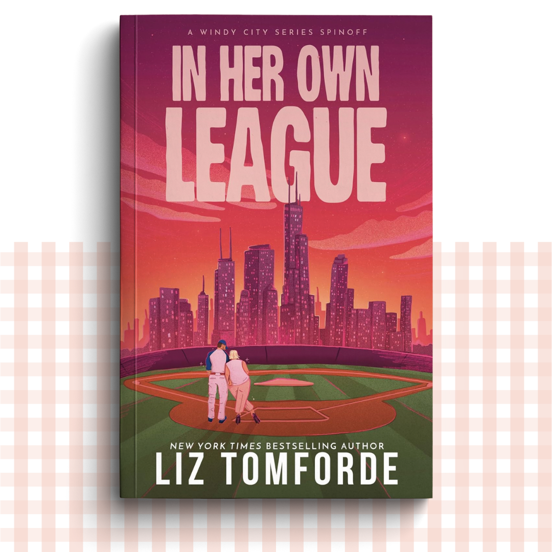 Paperback book cover of 'In Her Own League' by Liz Tomforde with a city skyline and couple on a baseball field.
