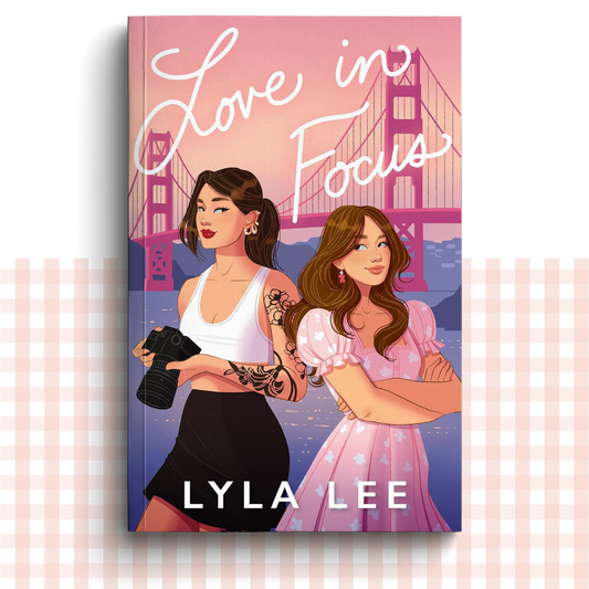 Paperback book cover of 'Love in Focus' by Lyla Lee with two women on the cover in front of a suspension bridge.